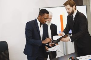Three businessmen engaged in document signing in a modern office setting. — 10 Benefits of Shopping at an Online Dispensary C