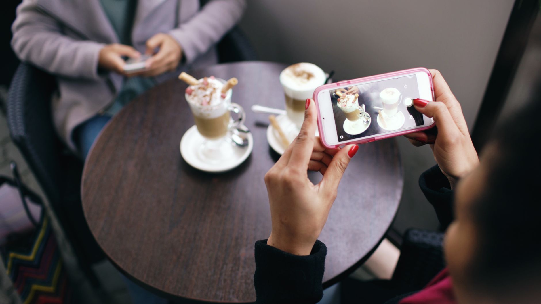 Two women in a cafe capturing photos of their coffee with smartphones. — 8 Advantages Of Using Social Media