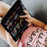 Young girl lying down using a tablet for entertainment and learning indoors. — Access Swedish and Global Entertainment Effort