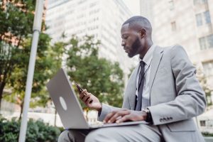 Businessman in a suit using a laptop and smartphone in an urban setting, blending technology with business. — Experience Peac