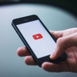 Close-up of a hand holding a smartphone displaying the YouTube app on the screen. — Experience the Thrill of Live Premier Lea