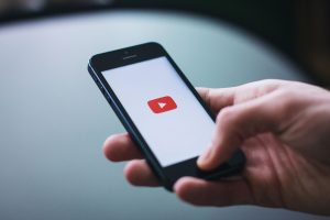 Close-up of a hand holding a smartphone displaying the YouTube app on the screen. — Experience the Thrill of Live Premier Lea