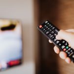 Close-up of a person using a TV remote with a blurred background indoors. — Experience the Thrill of the Game With Seamless S