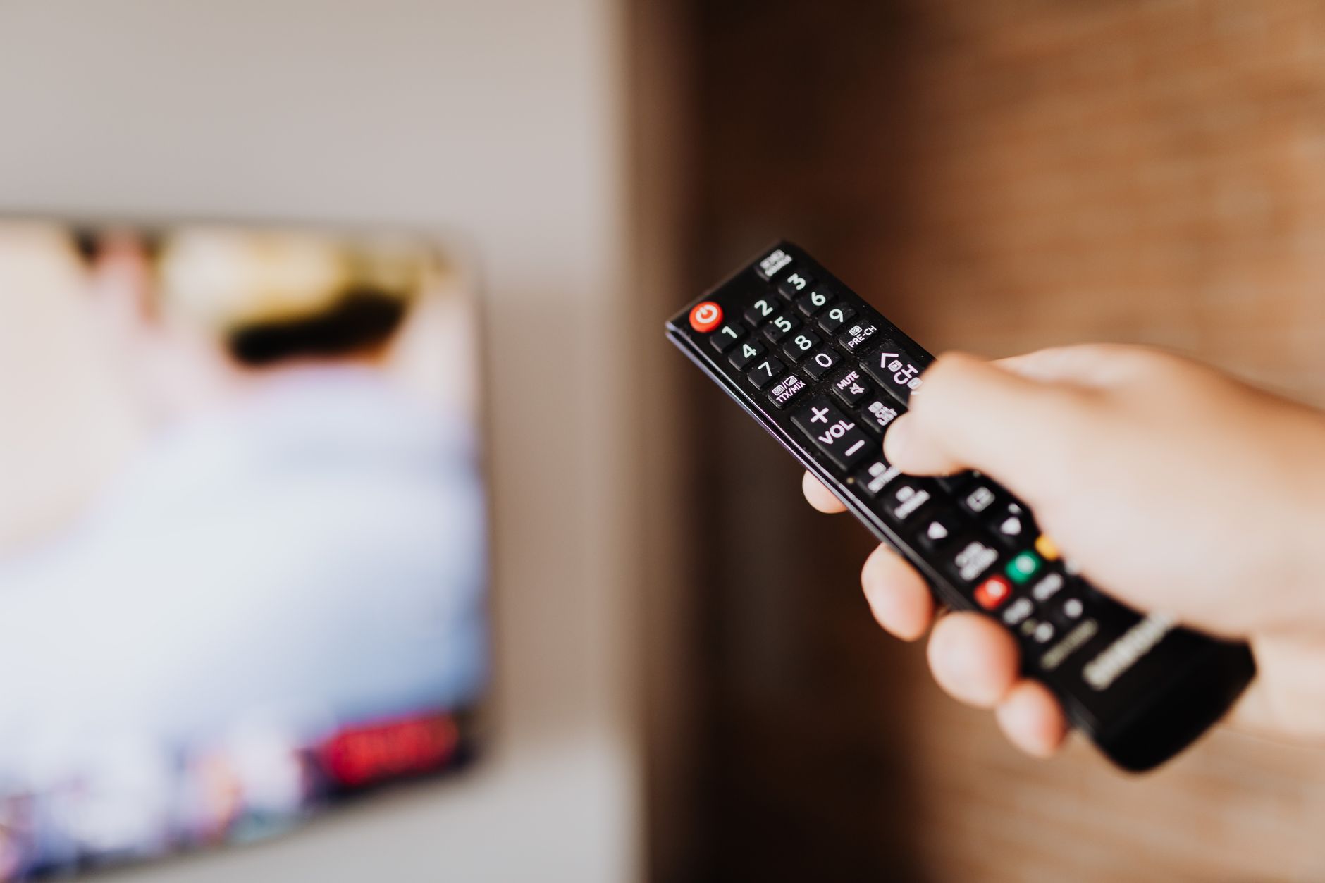 Close-up of a person using a TV remote with a blurred background indoors. — Experience the Thrill of the Game With Seamless S