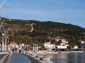 A beautiful coastal promenade in Foça, İzmir with a hillside backdrop, perfect for a relaxing stroll. — How can you save up y