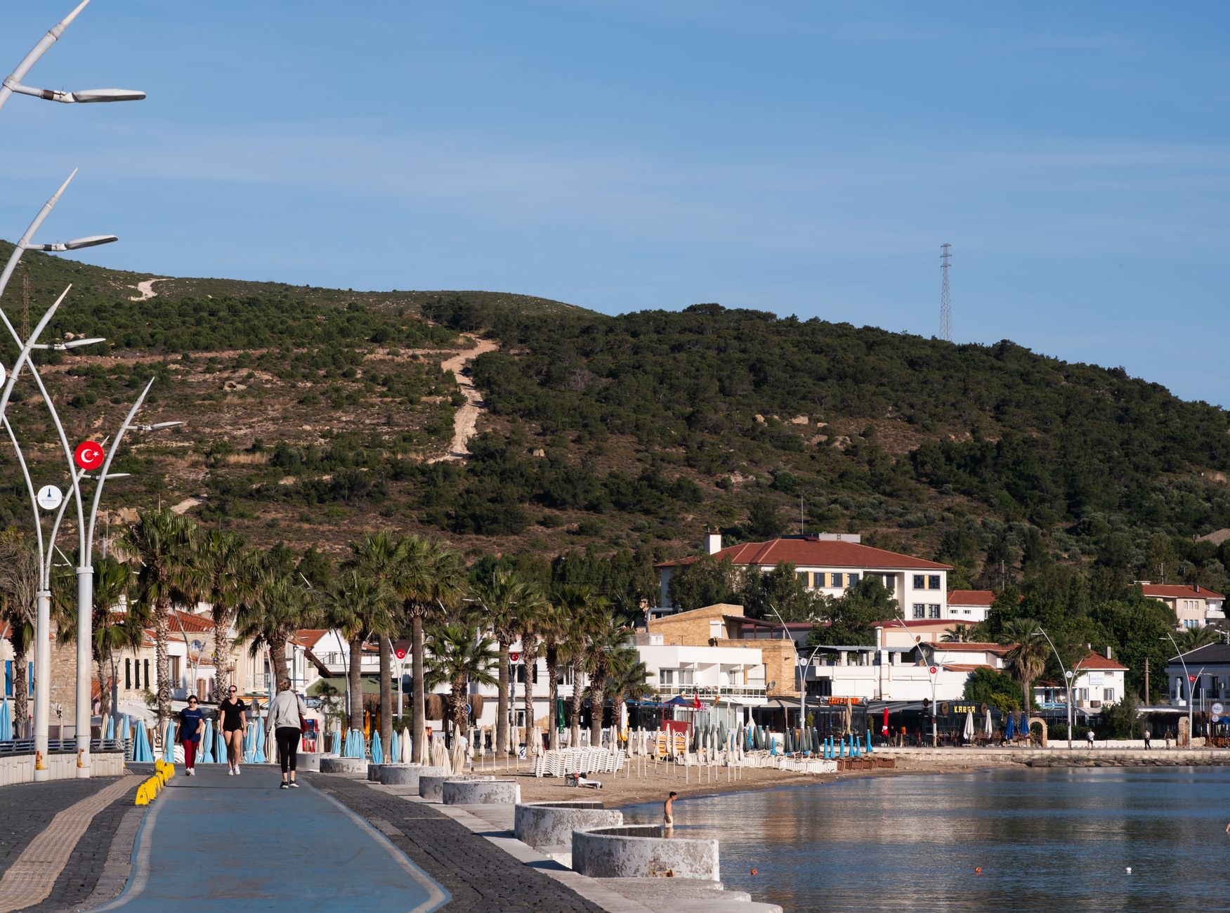 A beautiful coastal promenade in Foça, İzmir with a hillside backdrop, perfect for a relaxing stroll. — How can you save up y
