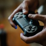 Crop anonymous male pressing buttons on console controller while playing video game in house on blurred background — Learning
