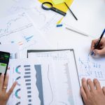Colleagues collaborating on financial charts and graphs using mobile and paper documents in the office. — Mastering Private M