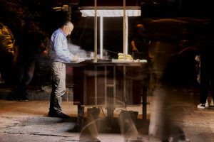 Street vendor cooking food at night with blurred people passing by. — NFLbite: Unrivalled Reddit NFL Streaming Platform
