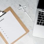 A clean and organized office desk setup featuring a laptop, clipboard with application form, and pen. — Securing Your Informa