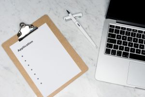 A clean and organized office desk setup featuring a laptop, clipboard with application form, and pen. — Securing Your Informa