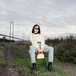 Stylish woman in sunglasses sitting by a bridge, showcasing modern fashion against a natural backdrop. — Analyzing Op