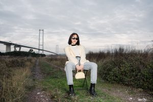 Stylish woman in sunglasses sitting by a bridge, showcasing modern fashion against a natural backdrop. — Analyzing Op