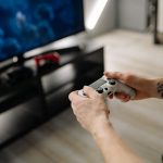 Person playing video games using a game controller indoors on a modern TV setup. — Beat the Best in Pokdeng Online wi