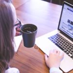 A woman enjoys coffee while browsing the web on a laptop at a home office desk. — The Lowdown on 4G Wireless Internet