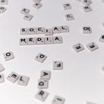 White Scrabble tiles forming the phrase 'social media' on a scattered background. — The Pros and Cons of Viewing Instagram St