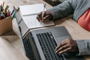 Crop unrecognizable African American female in formal wear writing notes in notepad while working on laptop — Unlock the Powe